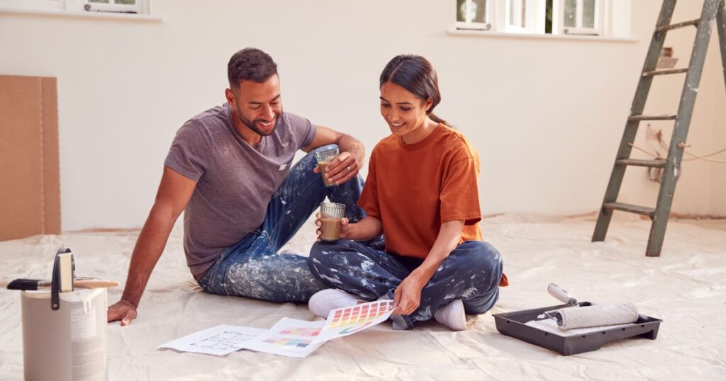 Couple Sitting On Floor With Paint Chart Ready To Decorate New Home