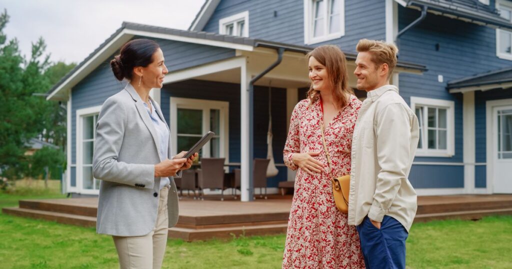 Young Couple Visiting a Potential New Home Property with Professional Real Estate Agent. Female real estate agent Showing the House to Future Homeowners. Focus on For Sale Sign.