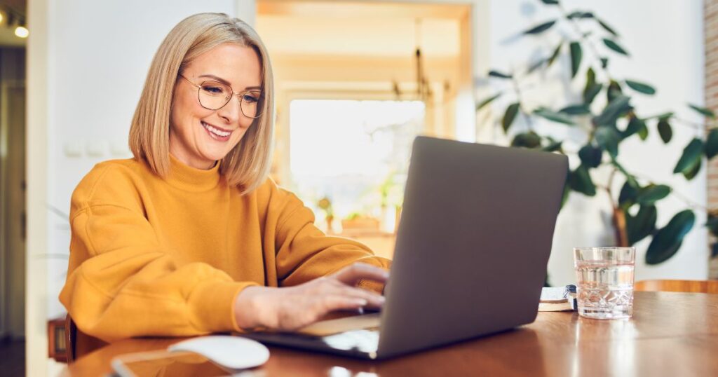 Cheerful mature woman working sitting at dinning table working from home office