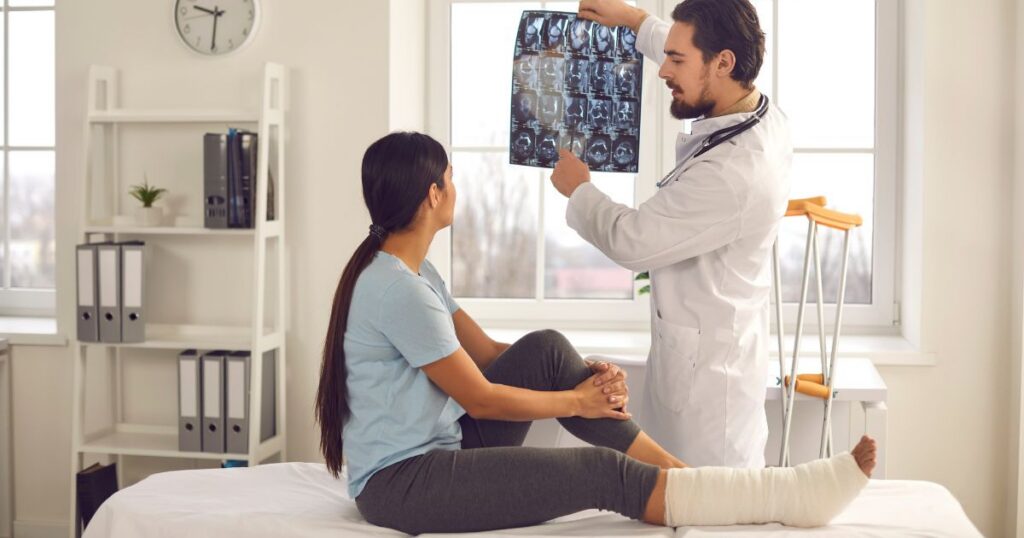 Woman listening to orthopedic doctor at hospital. Trauma surgeon or radiologist talking to patient, showing broken leg or foot fracture X-ray film, explaining treatment course, giving recovery