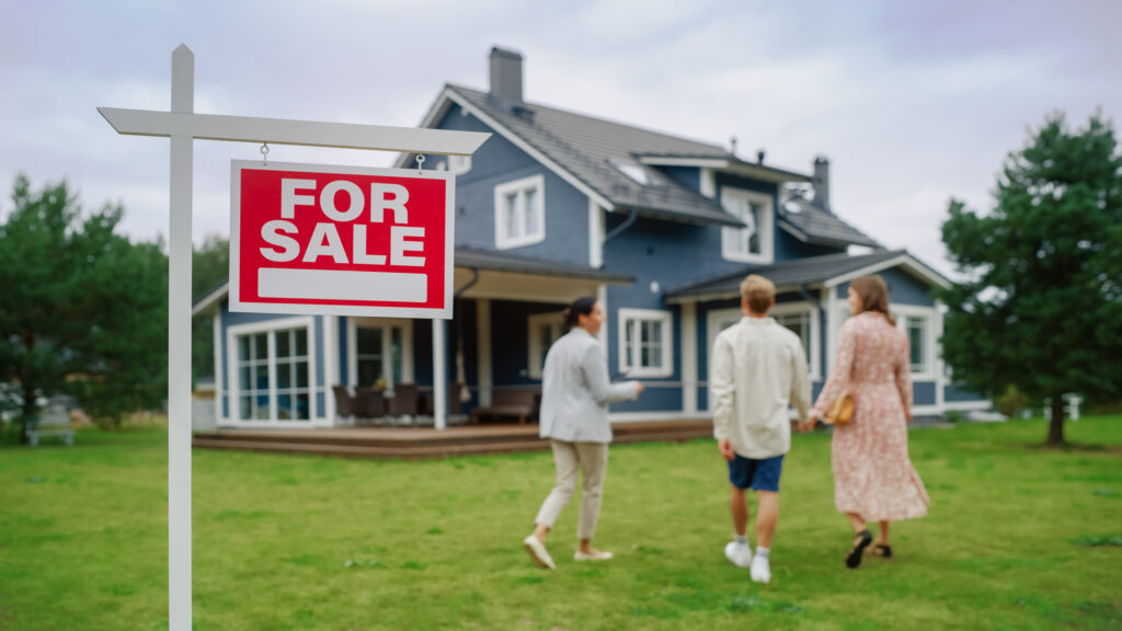 real estate agent Meeting a Beautiful Successful Couple in Front of a Modern Big House That is For Sale. Real Estate Agent Selling or Renting Out a New Home to a Young Family. For Sale Sign on Front Lawn.